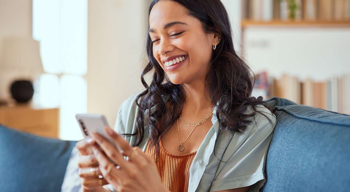 Customer smiling while scheduling a laundry pickup on a mobile phone at home.